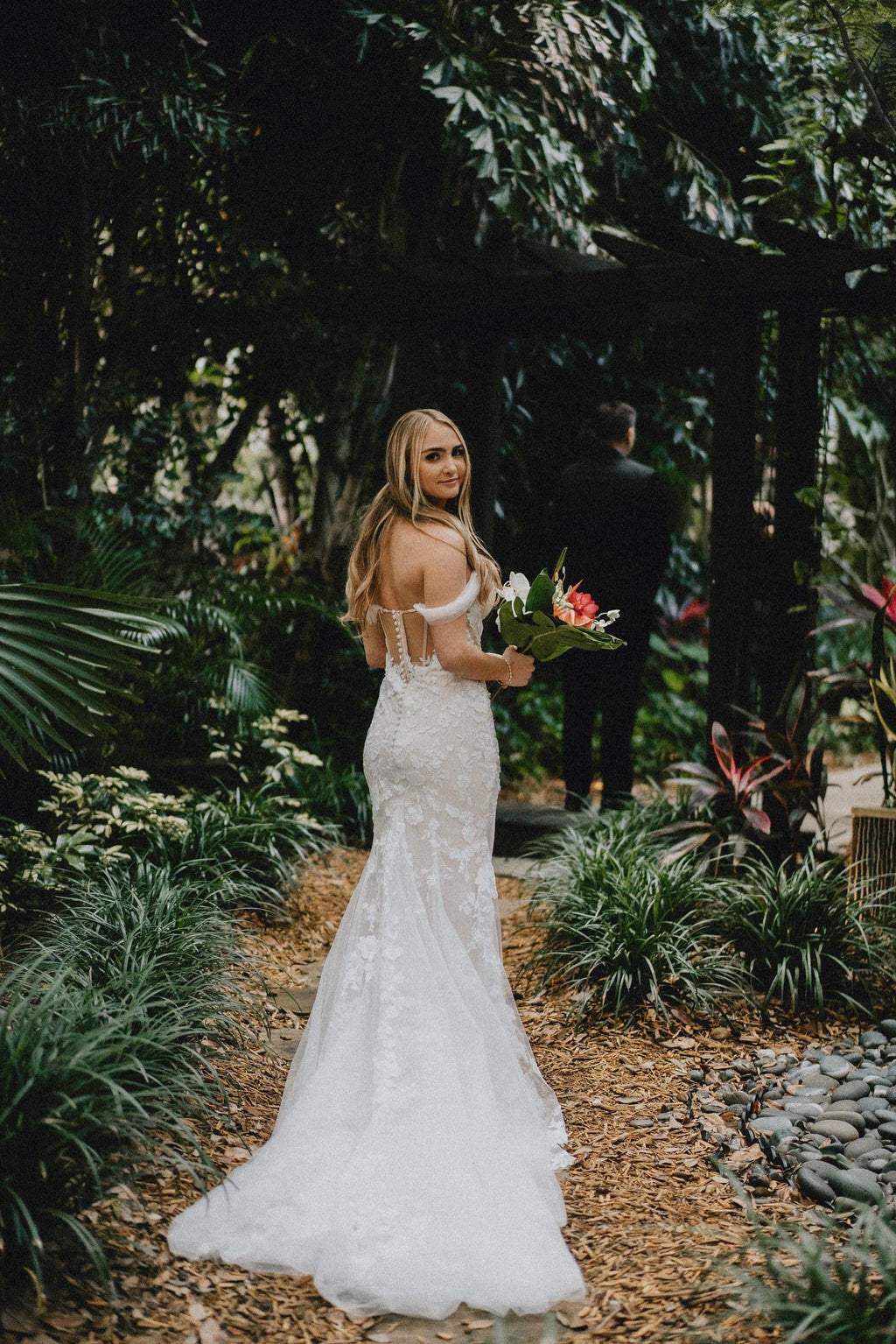 Bride in a beautiful lace wedding dress holding flowers in a garden.