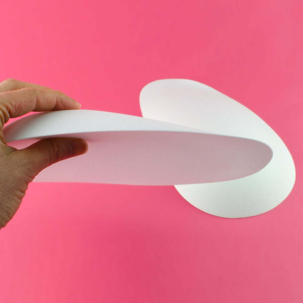 Hand holding foam butt pads against a pink background, showcasing the oblong shape of the butt pads.